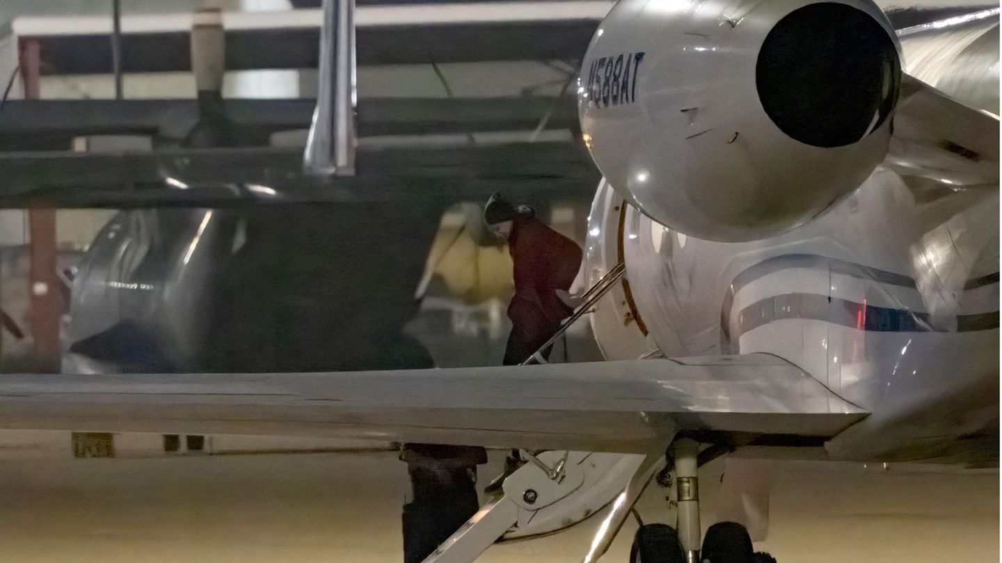Aus großer Entfernung ist eine Frau zu sehen, die in gebückter Haltung die Gangway eines Learjets hinuntergeht