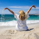 Eine Frau hebt am Strand auf Sardinien mit Sand gefüllte Hände in die Luft.
