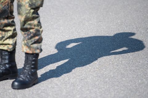 Tarnfleck-Hose und schwarze Stiefel eines Bundeswehr-Soldaten sind links im Bild, auf den Asphalt hinter ihm fällt sein Schatten