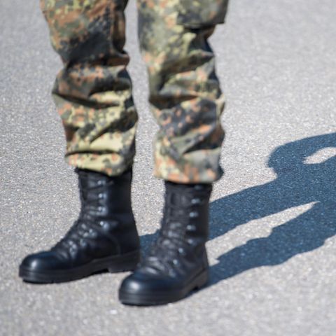 Tarnfleck-Hose und schwarze Stiefel eines Bundeswehr-Soldaten sind links im Bild, auf den Asphalt hinter ihm fällt sein Schatten