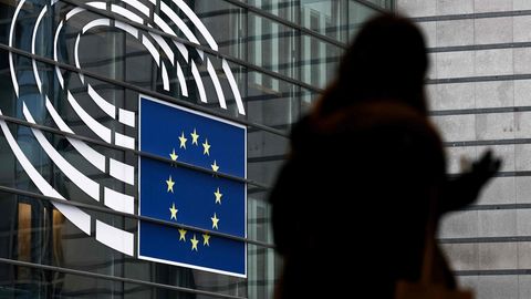 Eine Frau, von der nur eine schattenartige Kontur zu sehen ist, geht vor der Glasfassade des Europäischen Parlamentes vorbei