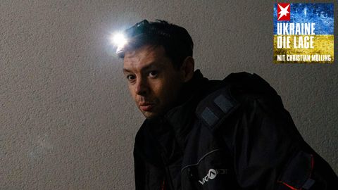 Ein weißer junger Mann mit einer angeschalteten Stirnlampe geht in einem dunklen Treppenhaus treppauf