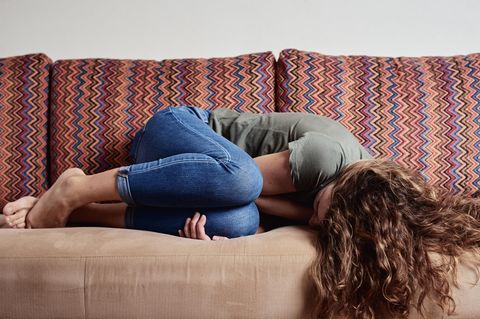 Eine Frau liegt gekrümmt auf dem Sofa.