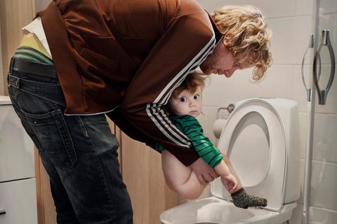 Väter können auch das: Vater hält sein Kleinkind über die Toilette