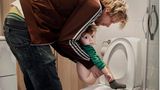 Vater hält seinen Sohn über der Toilette