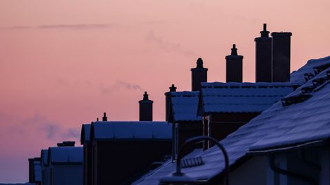 Vor einem Abendhimmel steigt Dampf aus den Schornsteinen einer Reihe Einfamilienhäuser mit Schnee auf den Dächern