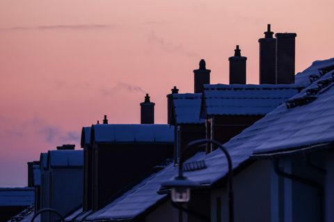 Vor einem Abendhimmel steigt Dampf aus den Schornsteinen einer Reihe Einfamilienhäuser mit Schnee auf den Dächern
