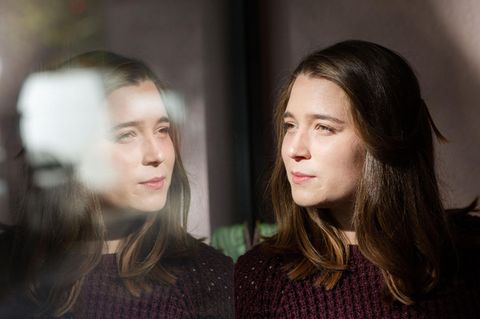 Emilia Fester schaut aus einem Fenster in dessen Scheibe sich ihr Gesicht spiegelt.