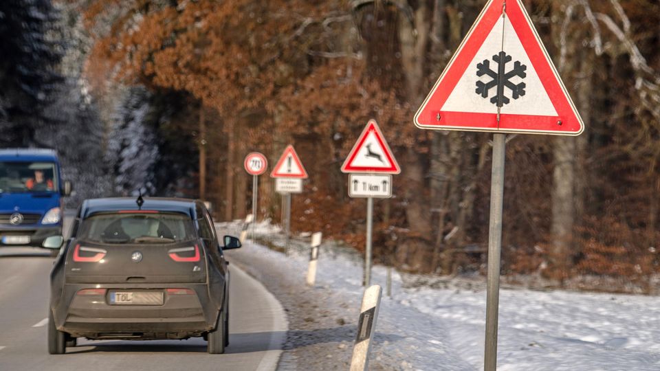 Ein Auto fährt an einem Verkehrsschild vorbei, das vor Schnee- oder Eisglätte warnt
