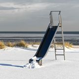 Eine einsame Rutsche wartet am verschneiten Nordseestrand von Schillig auf wärmere Zeiten