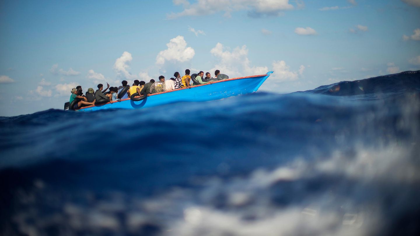 Migranten sitzen in einem Holzboot südlich der italienischen Insel Lampedusa auf dem Mittelmeer.