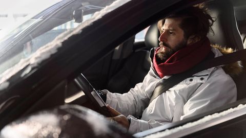 Ein Mann sitzt mit einer Jacke in einem Auto und hält seine Hände ans Lenkrad. Der ADAC testete Heizungen von E-Autos.