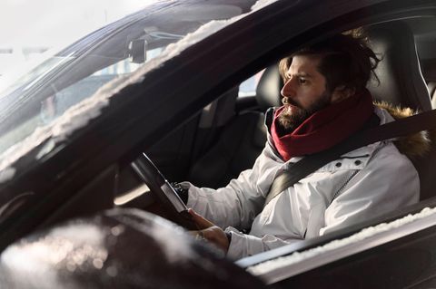 Ein Mann sitzt mit einer Jacke in einem Auto und hält seine Hände ans Lenkrad. Der ADAC testete Heizungen von E-Autos.