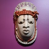 Eines der wertvollsten Stücke der Benin-Bronzen in Deutschland ist diese Miniatur-Elfenbeinmaske. Es gibt nur etwa vier vergleichbare Stücke auf der Welt. Museumsaufzeichnungen zufolge wurde sie 1897 im Schlafgemach des regierenden Königs Ovonramwen gefunden und gestohlen. Es wurde also offensichtlich jahrhundertelang als Ahnenobjekt verehrt und bewacht. Dargestellt ist die Königinmutter ("Iyoba") Idia, die Mutter des 17. Oba Esigie (regierte 1504-1550).