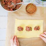 Maultaschen füllen: Den Teig mit einem Nudelholz etwa 0,8 mm dünn zu einem Rechteck ausrollen. Die Füllung mittig und immer mit etwas Abstand auf die ganze Länge des Teigs verteilen. Dann den oberen und unteren Rand des Teigs mit Wasser bestreichen.