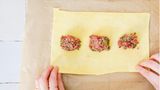 Maultaschen füllen: Den Teig mit einem Nudelholz etwa 0,8 mm dünn zu einem Rechteck ausrollen. Die Füllung mittig und immer mit etwas Abstand auf die ganze Länge des Teigs verteilen. Dann den oberen und unteren Rand des Teigs mit Wasser bestreichen.