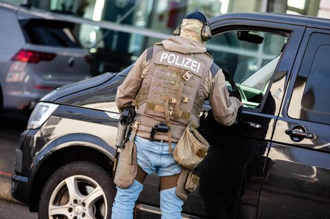 Ein Mann mit Polizei-Schutzweste und Waffen im Holster spricht durch das Fenster eines VW-Buses mit der Person am Steuer