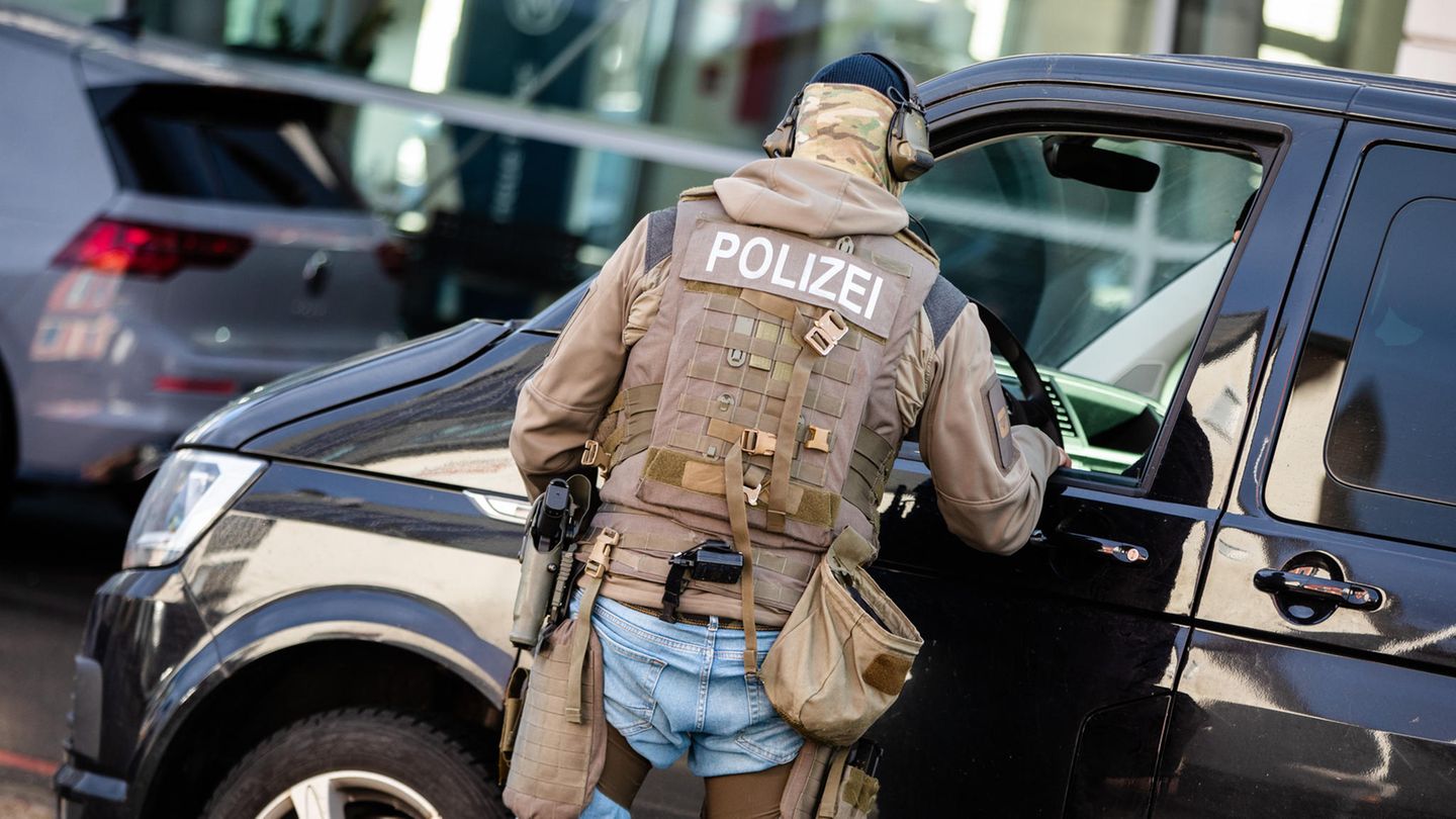Ein Mann mit Polizei-Schutzweste und Waffen im Holster spricht durch das Fenster eines VW-Buses mit der Person am Steuer