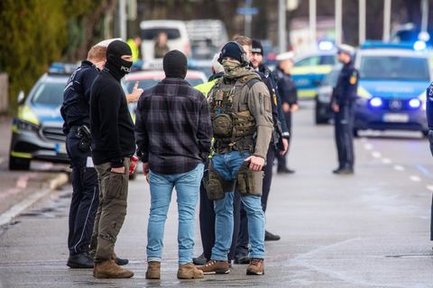 Einsatzkräfte der Polizei stehen nahe eines Tatorts auf der Straße