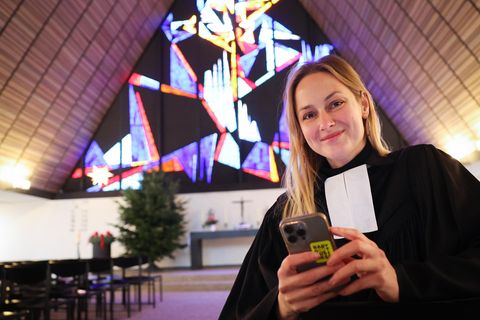 Die junge Pastorin Josephine Teske steht in einer Kirche und hält ihr Smartphone in der Hand