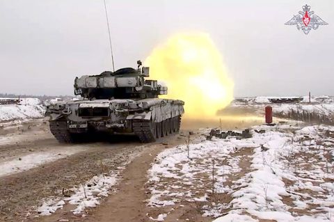 Auf einem verschneiten Feldweg ist ein Panzer von hinten zu sehen, als er gerade schießt und ein Feuerball vor ihm scheint
