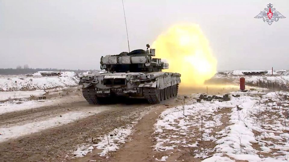 Auf einem verschneiten Feldweg ist ein Panzer von hinten zu sehen, als er gerade schießt und ein Feuerball vor ihm scheint