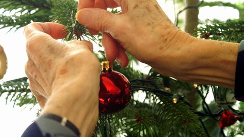 Eine Person hängt einen Weihnachtskugel an einen Tannenbaum