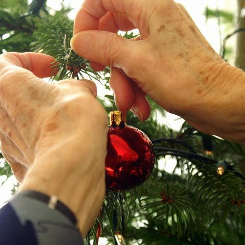 Eine Person hängt einen Weihnachtskugel an einen Tannenbaum