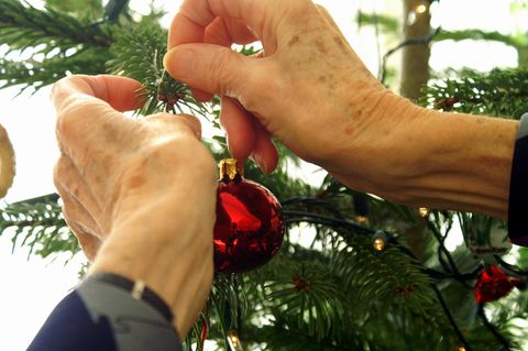 Eine Person hängt einen Weihnachtskugel an einen Tannenbaum