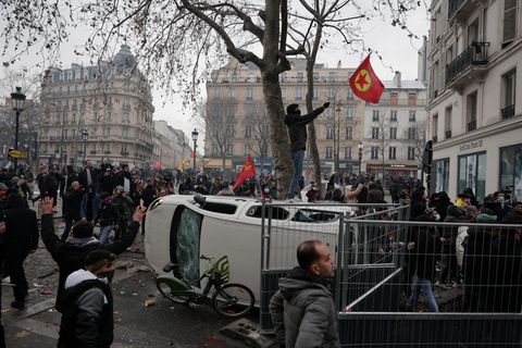Frankreich, Paris: Ein Demonstrant steht auf einem umgekippten Auto und schwenkt eine Fahne der Arbeiterpartei Kurdistans (PKK), während eines Protestes nach Schüssen in einem Kulturzentrum in Paris.