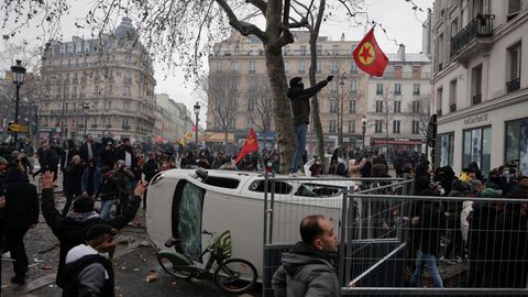 Frankreich, Paris: Ein Demonstrant steht auf einem umgekippten Auto und schwenkt eine Fahne der Arbeiterpartei Kurdistans (PKK), während eines Protestes nach Schüssen in einem Kulturzentrum in Paris.