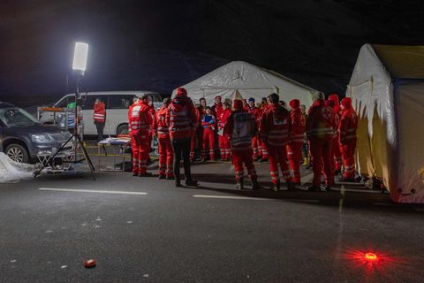Im Licht eines Scheinwerfers stehen Rettungskräfte in roter Kleidung vor zwei Großzelten