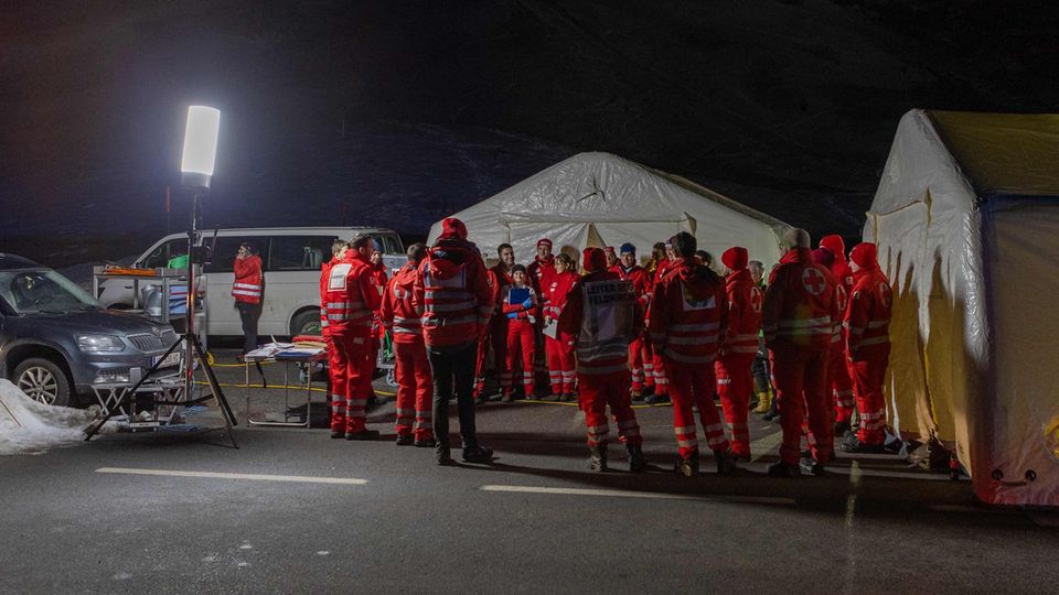 Im Licht eines Scheinwerfers stehen Rettungskräfte in roter Kleidung vor zwei Großzelten