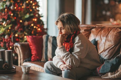 Eine Frau sitzt traurig auf dem Sofa vor dem Weihnachtsbaum