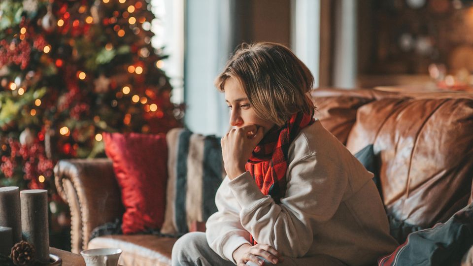 Eine Frau sitzt traurig auf dem Sofa vor dem Weihnachtsbaum
