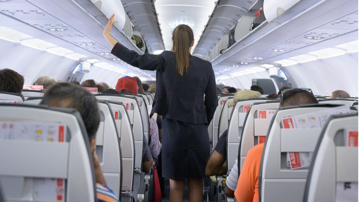 Eine Flugbegleiterin ist von hinten zu sehen, wie sie im Gang eines Flugzeugs steht