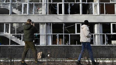 Zwei Menschen fotografieren im Vorbeigehen ein von Raketen getroffenes Gebäude in Kiew