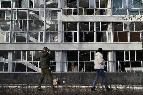 Zwei Menschen fotografieren im Vorbeigehen ein von Raketen getroffenes Gebäude in Kiew