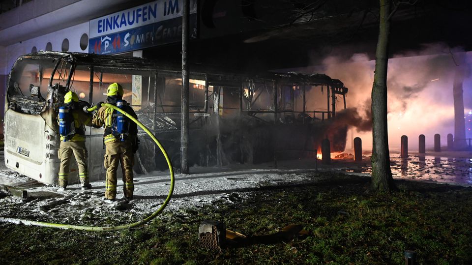 Feuerwehrmänner löschen an der Sonnenallee einen Reisebus, der von Unbekannten angezündet worden war.