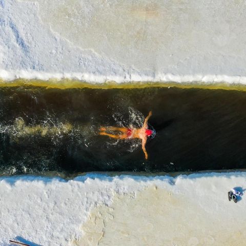Eisschwimmer zieht seine Bahnen im zugefrorenen Fluss Yimin