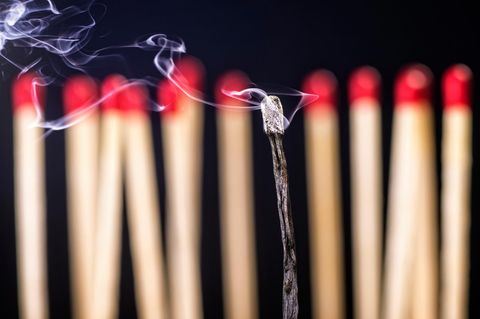 Burnout-Symbolbild: Mehrere unangezündete Streichhölzer in einer Reihe im Hintergrund, im Vordergrund ein abgebranntes