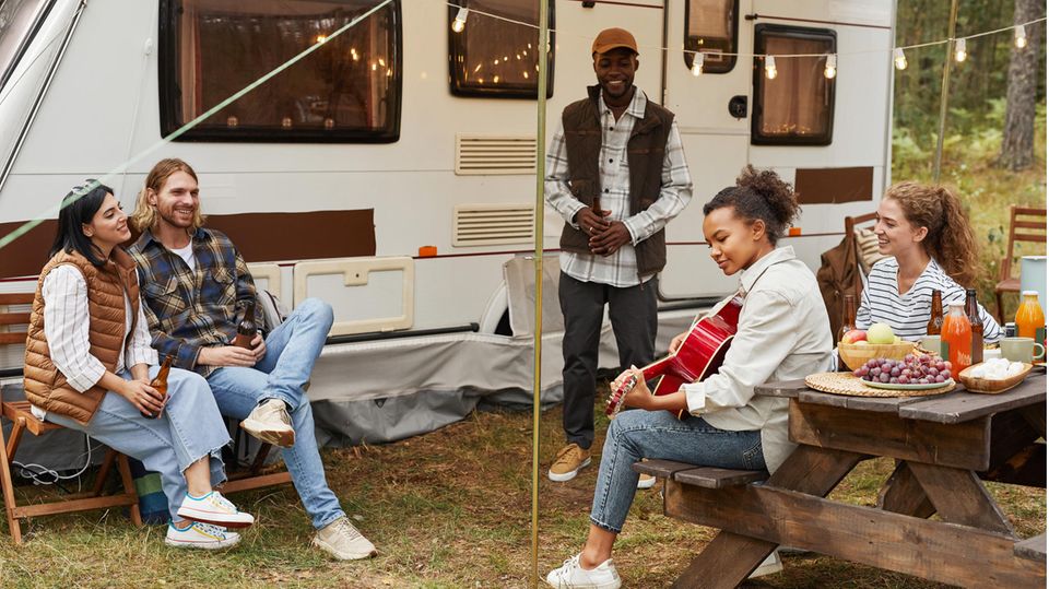 Eine Gruppe junger Menschen sitzt vor einem Wohnwagen.