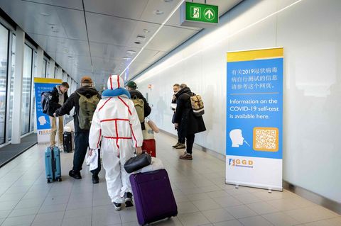 Reisende aus in China gehen auf dem Amsterdamer Flughafen Schiphol an Informationsbannern vorbei