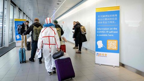 Reisende aus in China gehen auf dem Amsterdamer Flughafen Schiphol an Informationsbannern vorbei