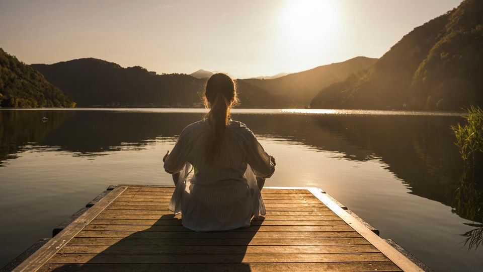 Eine Frau mit Autoimmunerkrankung sitz entspannt an einem See