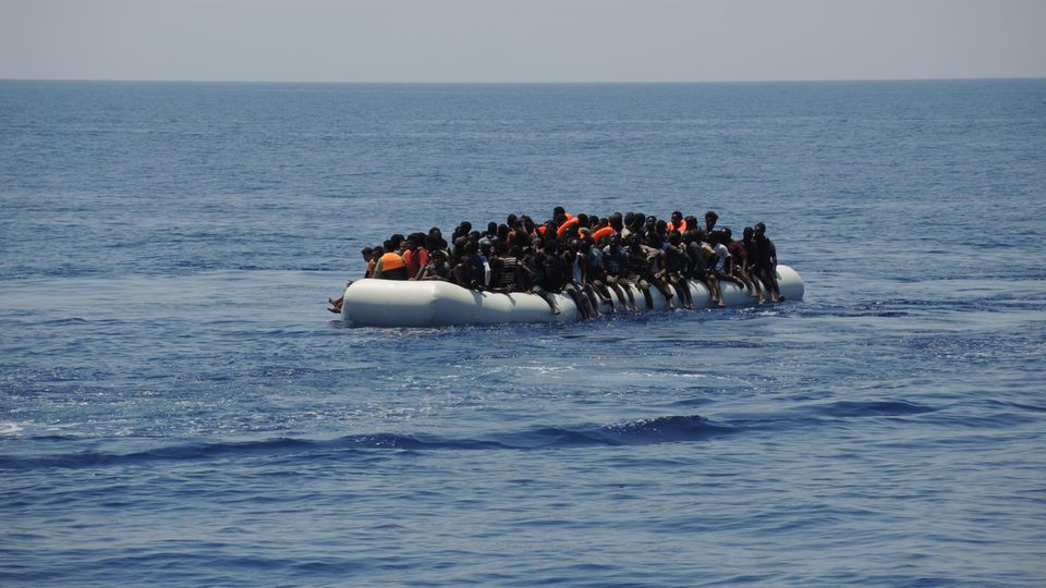 Migranten sitzen eng an eng auf einem Schlauchboot auf dem Mittelmeer