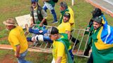 Ein verletzter Angreifer wird von anderen Bolsonaro-Anhängern auf einem Absperrgitter davongetragen