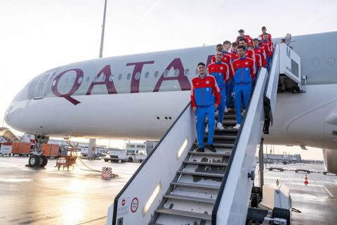 Fußballer in rot-blauen Trainingsanzügen stehen auf einer Gangway zu einem Flugzeug mit "Qatar Airways"-Lackierung