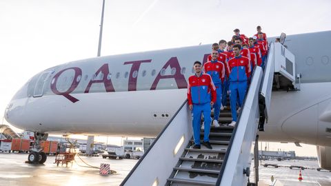 Fußballer in rot-blauen Trainingsanzügen stehen auf einer Gangway zu einem Flugzeug mit "Qatar Airways"-Lackierung