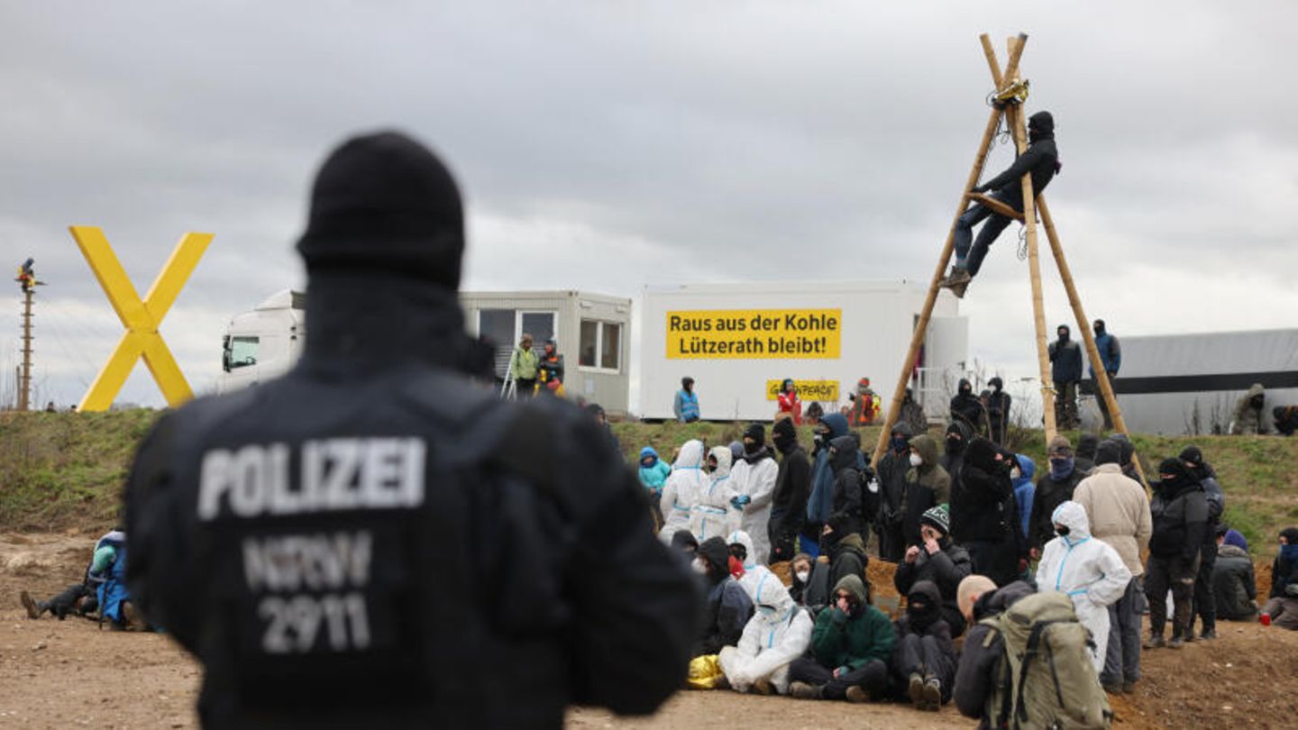 Ein Polizist beobachtet Klimaschutzaktivisten. die am Rand des Tagebaus sitzen